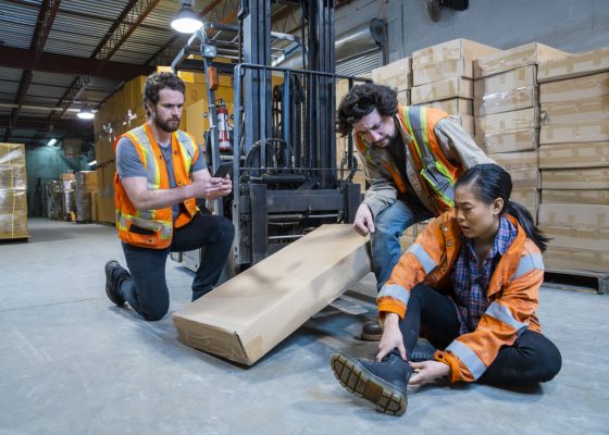 An industrial warehouse workplace safety topic. A worker injured falling or being struck by a forklift.